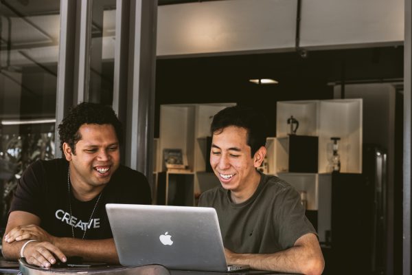 Two men working on a Mac laptop and smiling at the screen